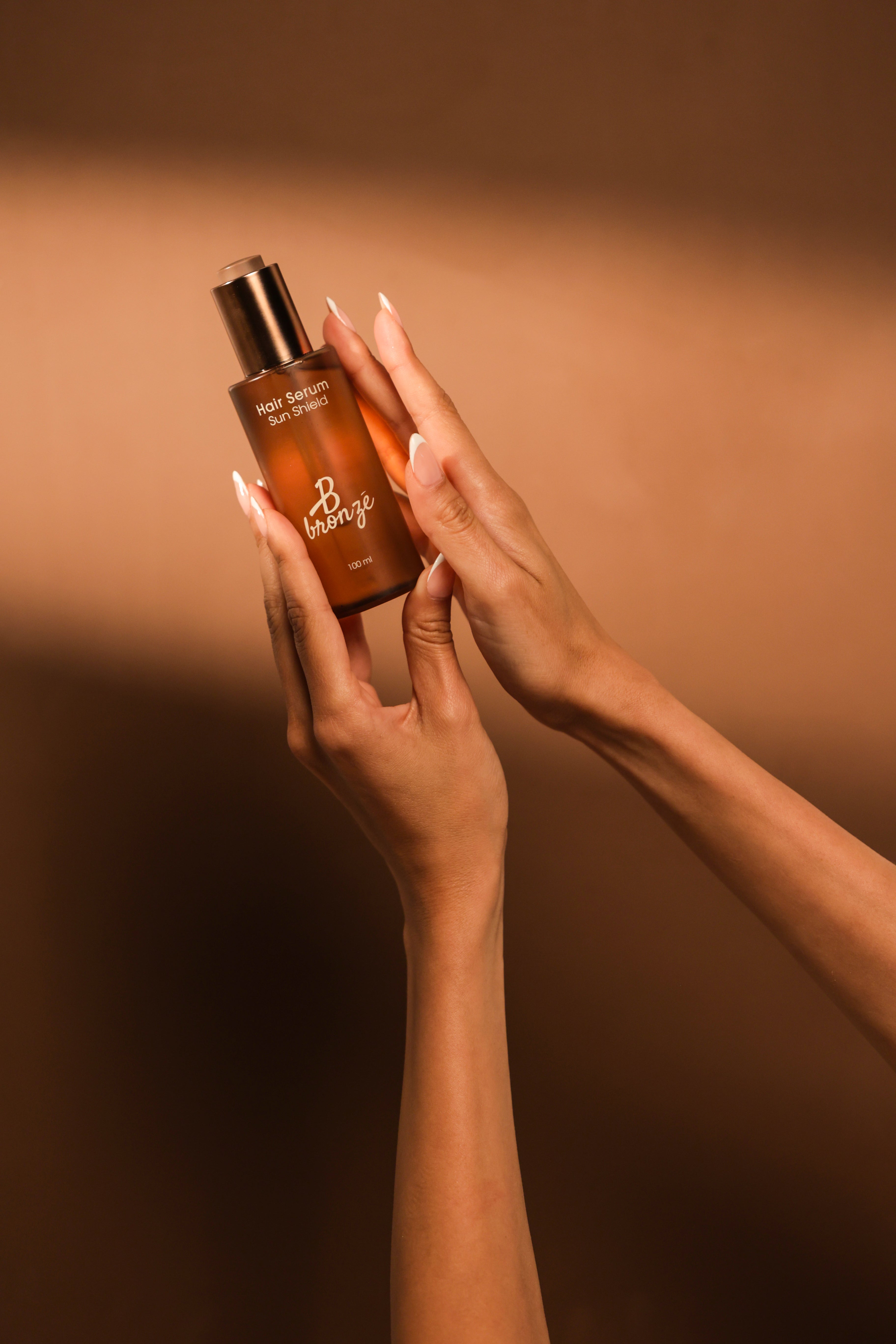 Hands holding the B Bronzé Sun Shield Hair Serum bottle