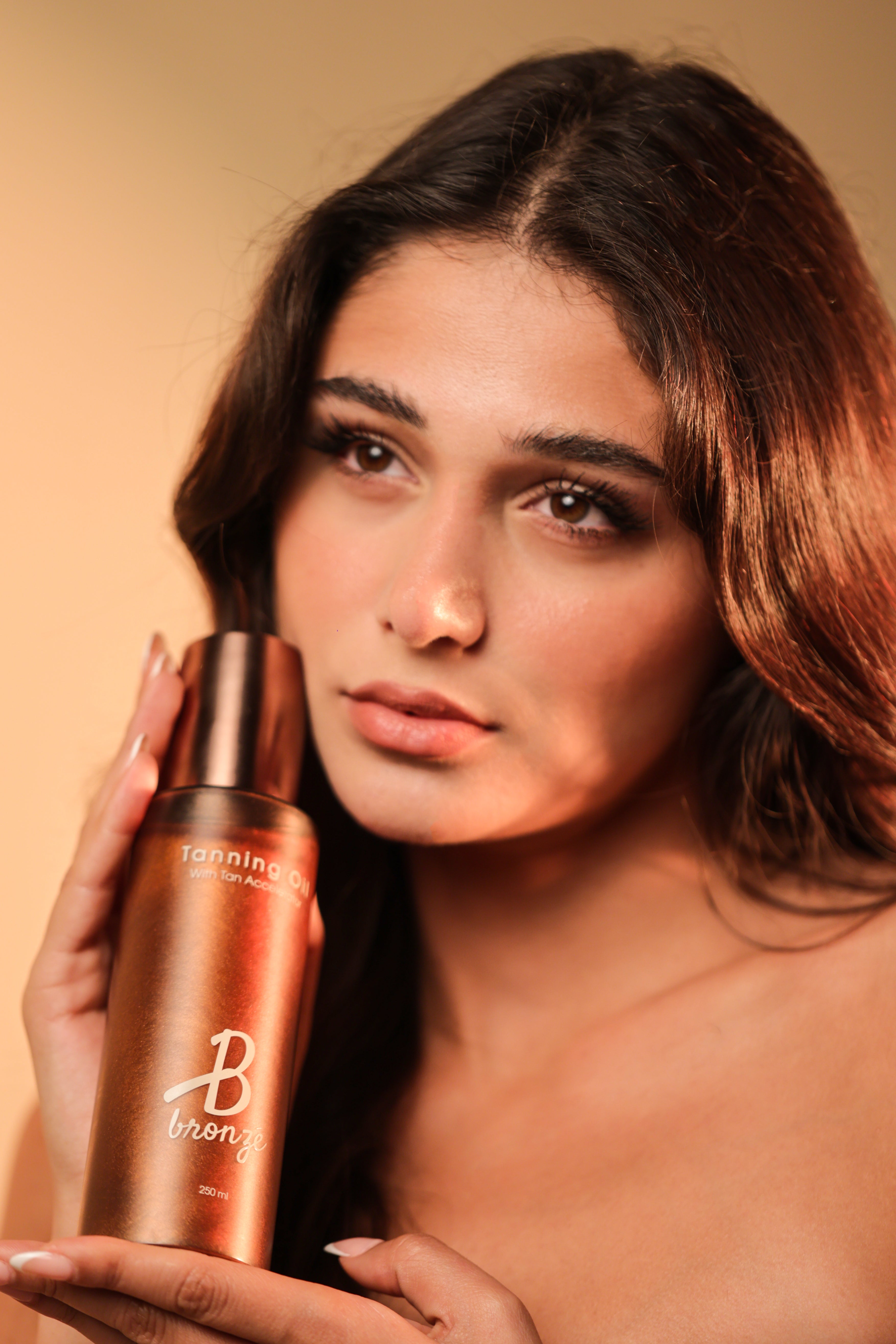 Model holding the B Bronzé Tanning Oil with Tan Accelerator bottle